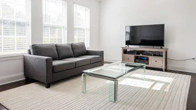 A clean living room with squared sofa cushions, a clear glass coffee table and a vacuumed rug