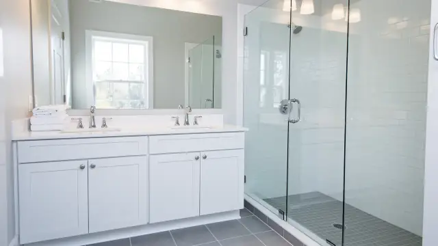 A clean bathroom with a white double vanity, chrome faucets and a glass shower