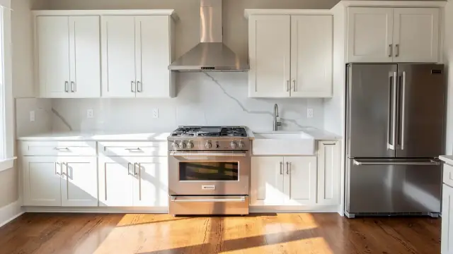A clean kitchen with a stainless range, white cabinets and a wiped quartz counter